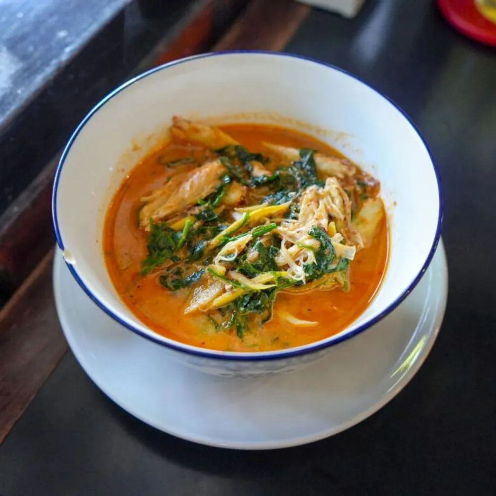 A bowl of red curry with shredded fish and holy basil.