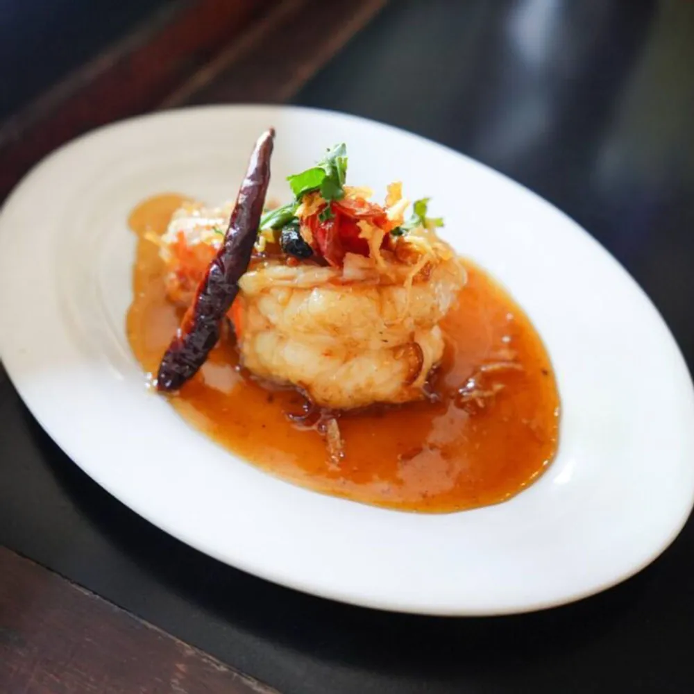 A fillet of fish under a red chilli sauce with a dried chilli on top.