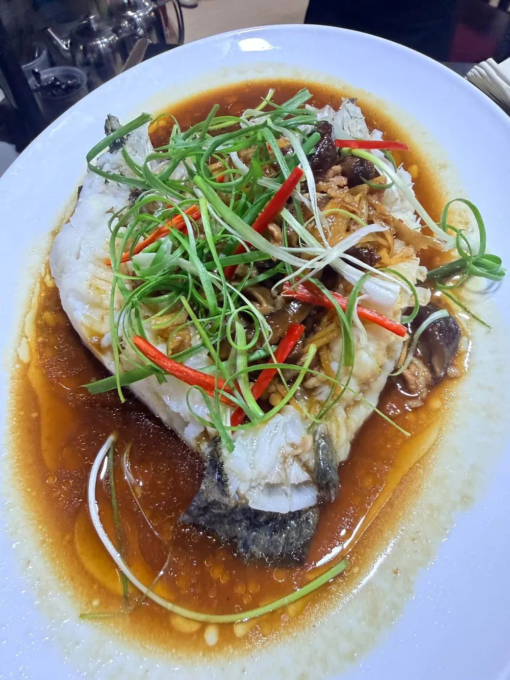 A whole steamed fish in soy sauce, topped with spring onion, ginger and red chilli.
