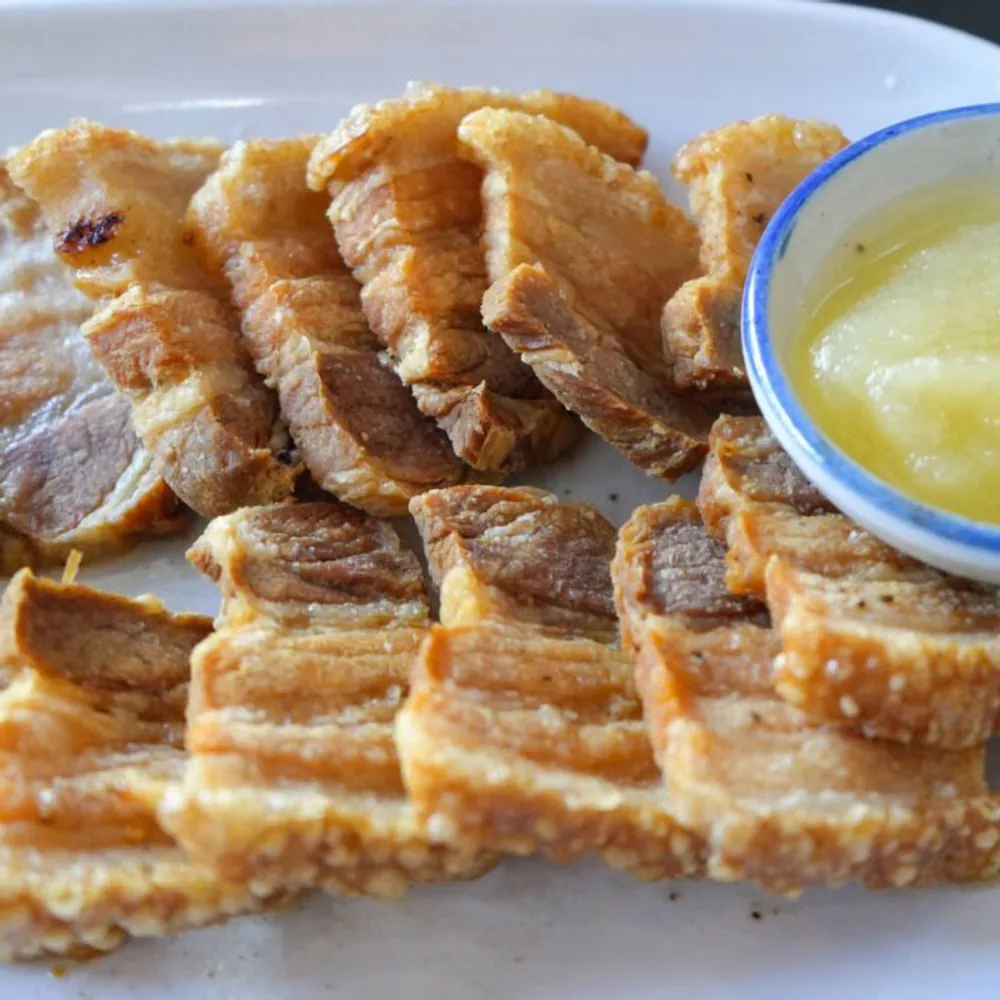 Slices of crispy pork belly with a bowl of pale apple sauce.