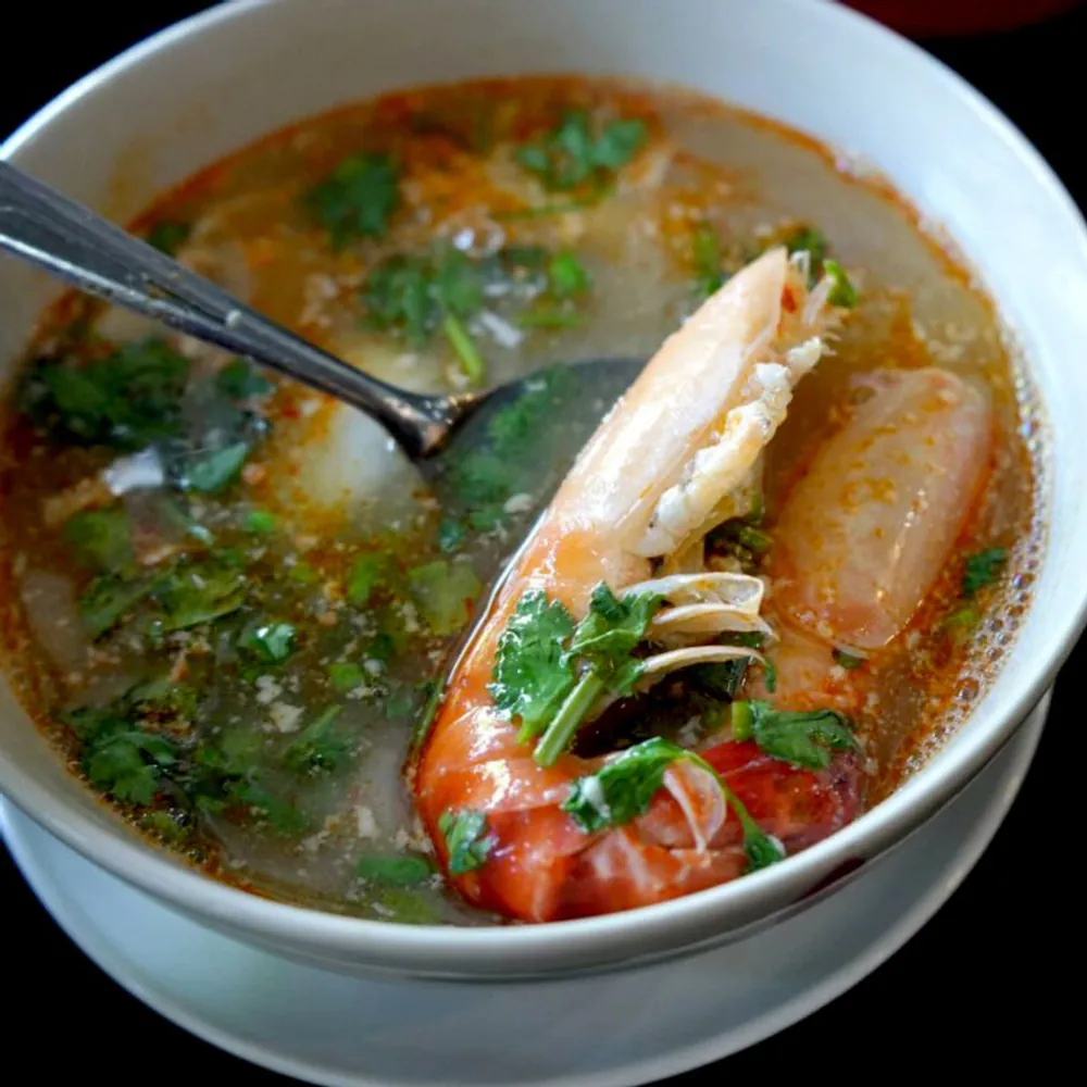 A bowl of tom yum with a whole prawn, coriander and pieces of young coconut.